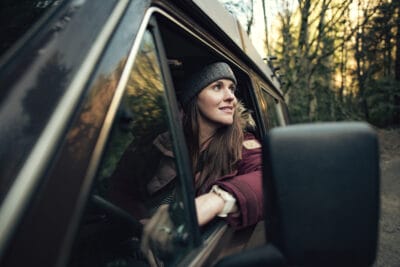 Girl looking out the window of a car, seemingly in the woods