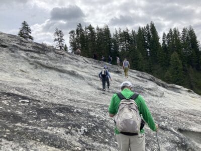 A group hikes up a large stone slab toward distant trees.
